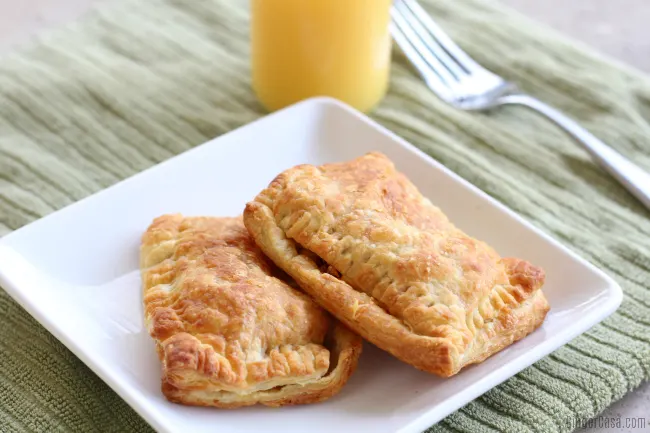 White plate with two breakfast pockets, a fork, and a glass of orange juice.