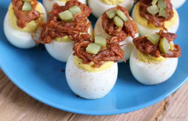 Blue plate with pulled pork deviled eggs, all topped with a pickle.