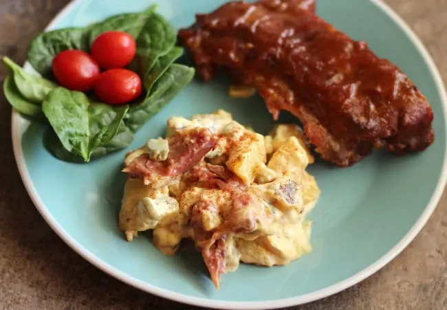 Teal plate with bbq rib potato salad, green salad with tomatoes, and bbq ribs.