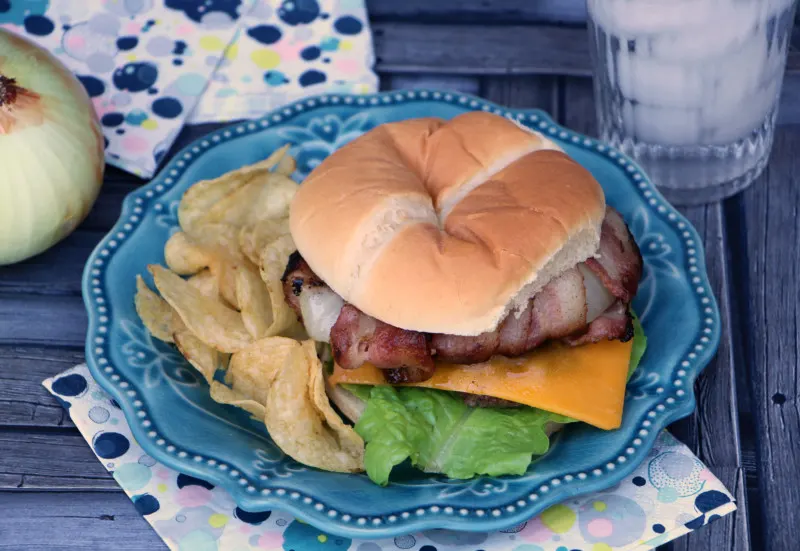 Blue plate with a cheeseburger and chips with an onion and glass of water in the background.