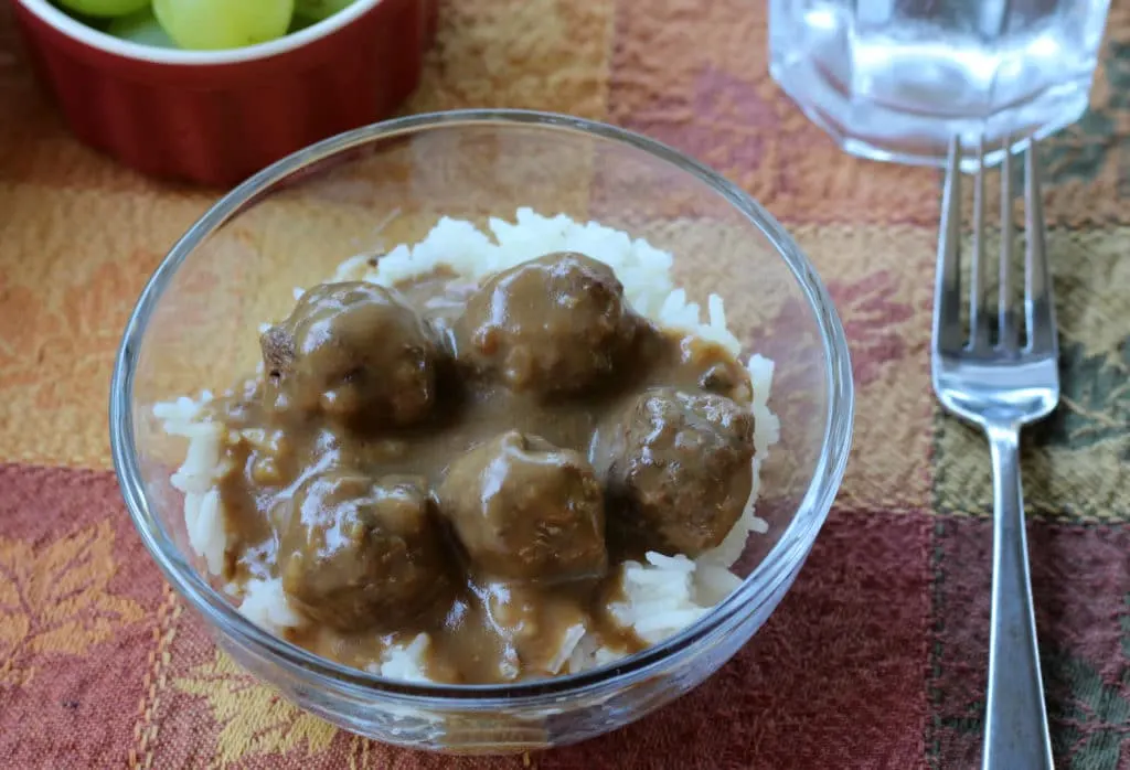 Glass bowl with meatballs and gravy over rice with a fork to the right side.