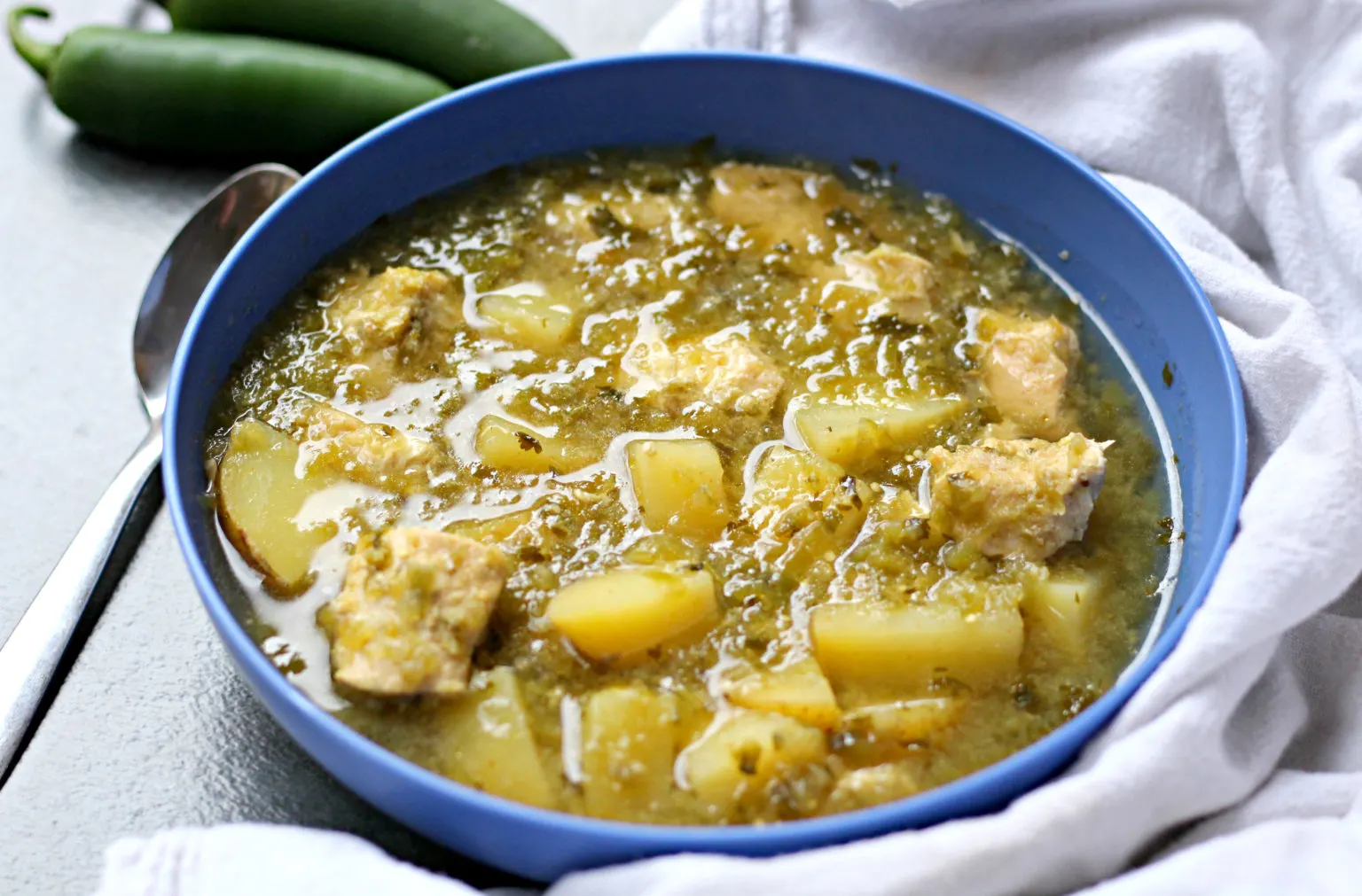 chicken verde with potatoes soup in a blue bowl with spoon