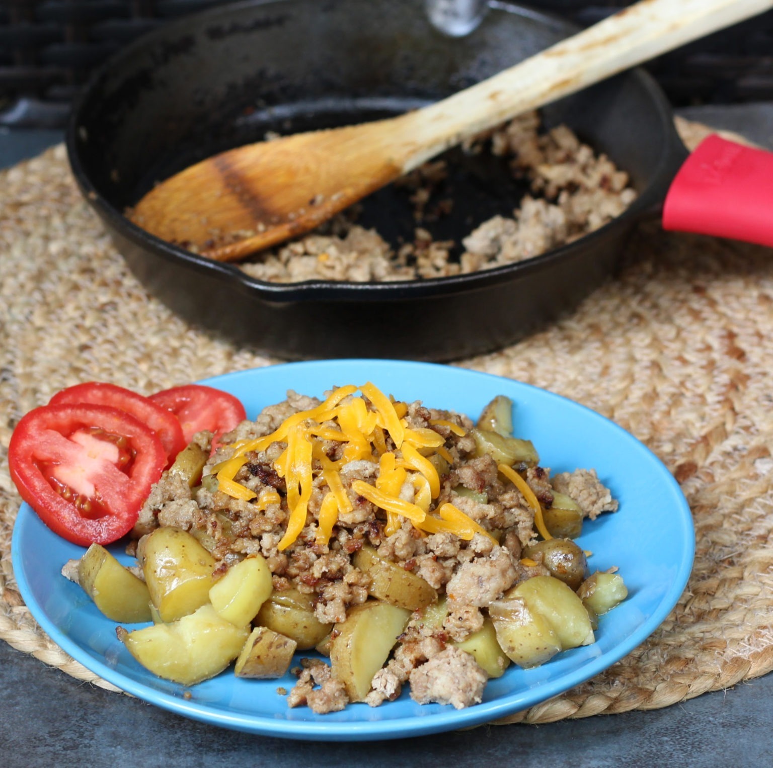 A blue plate with meat, potatoes and tomatoes.