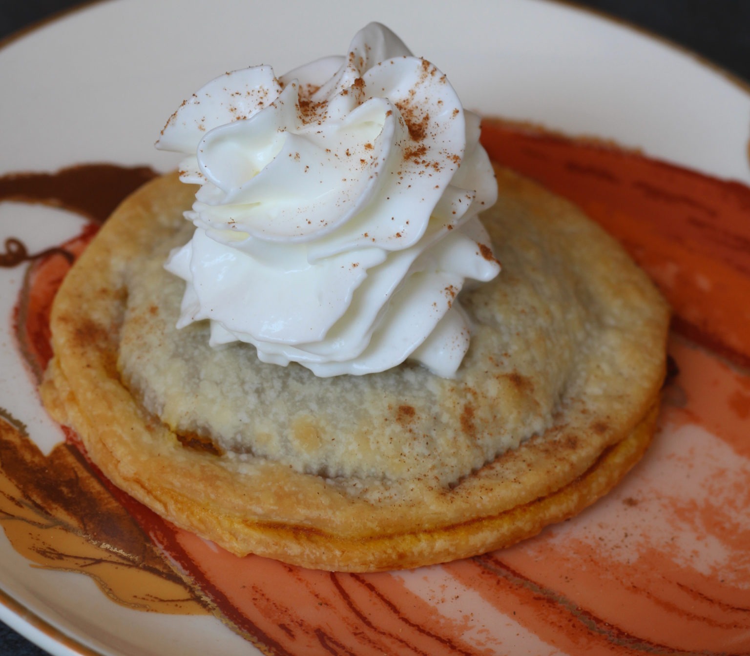 Pumpkin pie pop tart with whipped cream on top on a pumpkin plate.