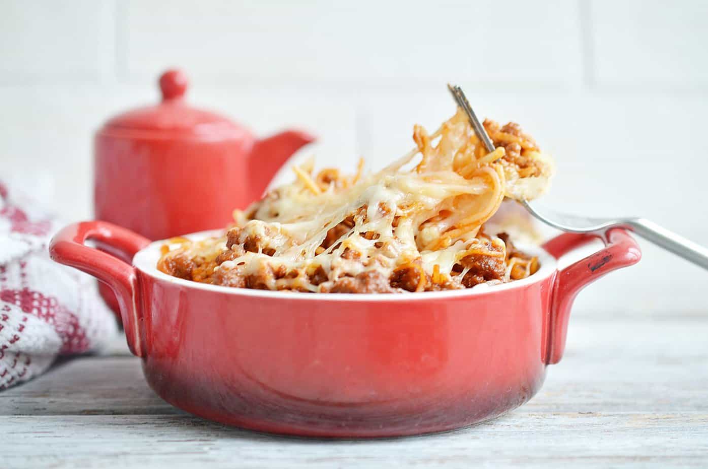 A red dish of spaghetti casserole with a fork in it, to the side.