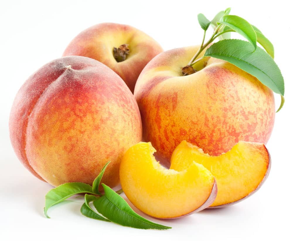 Ripe peach fruit with leaves and slices on white background.
