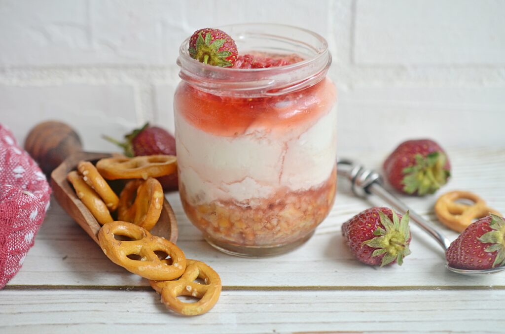layered strawberry pretzel salad in a jar with pretzels and strawberries to the side