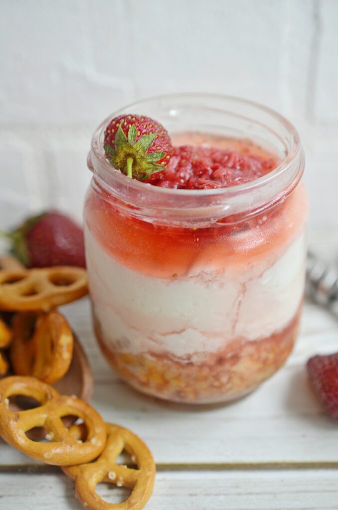 closeup of layered strawberry pretzel salad in a jar with pretzels and strawberries to the side