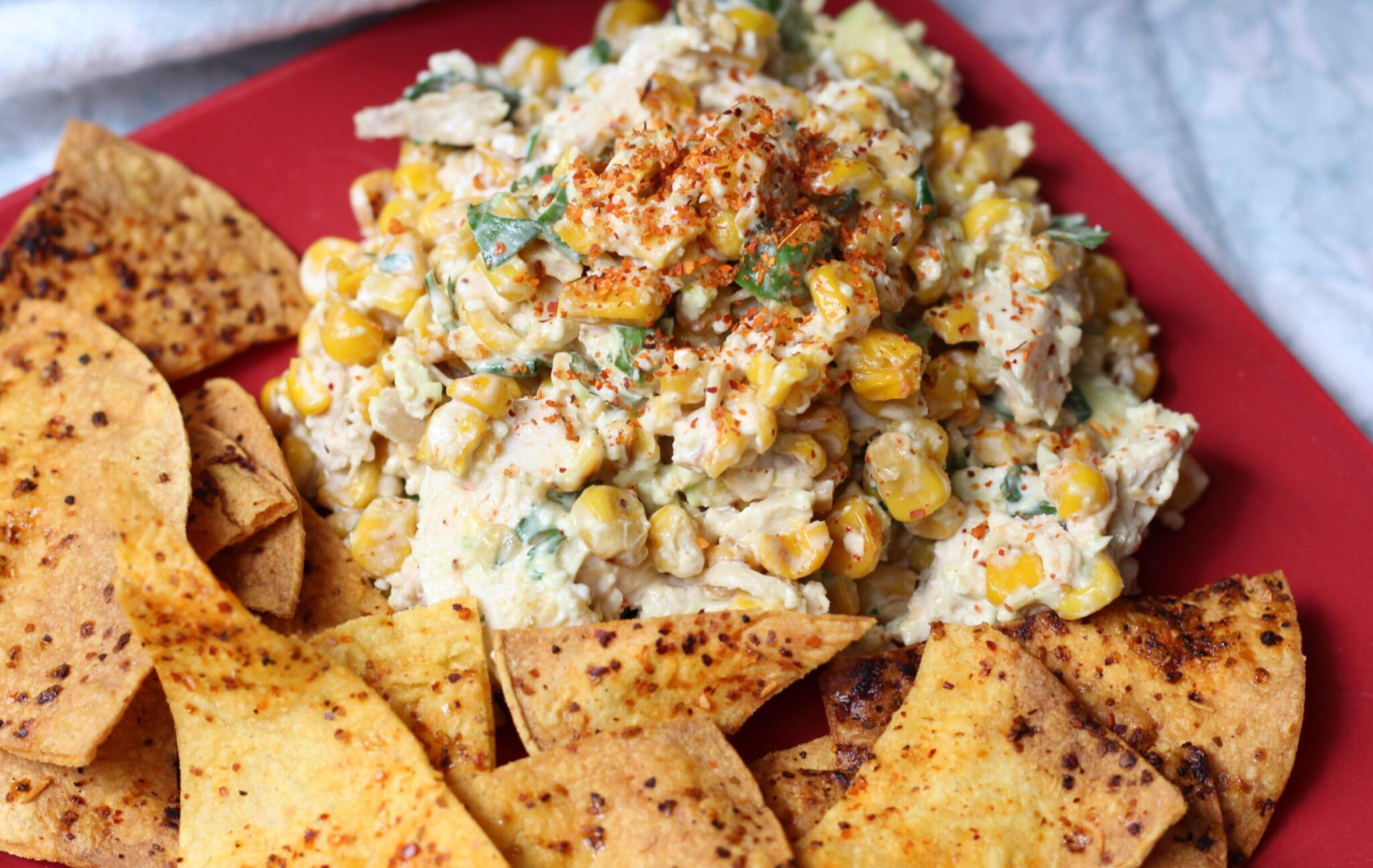 Red plate with chicken salad and chips.